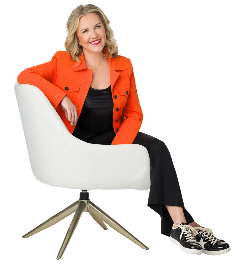 Molly, a smiling blonde woman, sits in a white office chair wearing an orange jacket, black pants, and sparkly black sneakers.