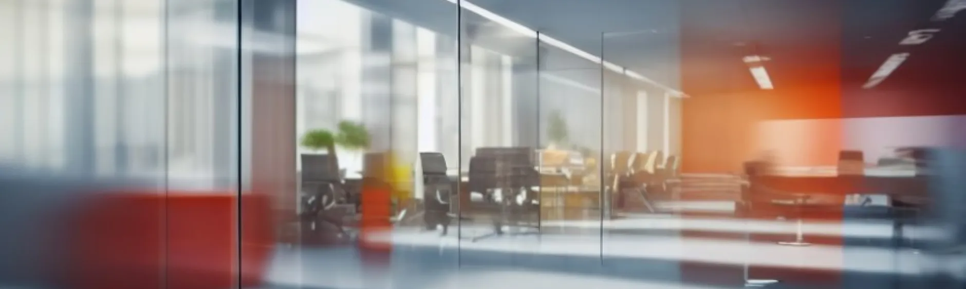 A modern conference room viewed through glass, featuring a table, chairs, and a small potted plant in warm ambient light.